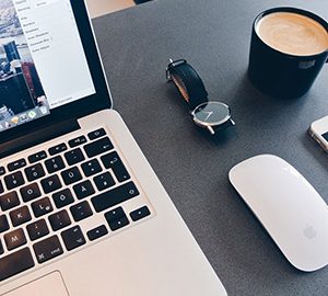 Un portable ouvert et bien rangé sur le côté il y a la souris une montre et une tasse de café