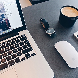 Un portable ouvert et bien rangé sur le côté il y a la souris une montre et une tasse de café
