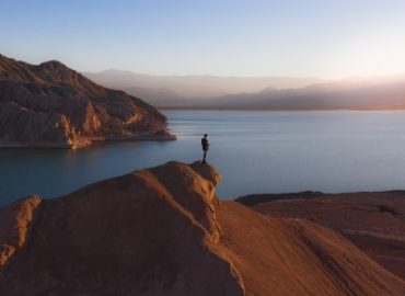 Une personne au-dessus d'une des montagnes brunes, sans arbre, avec la mer en arrière plan.