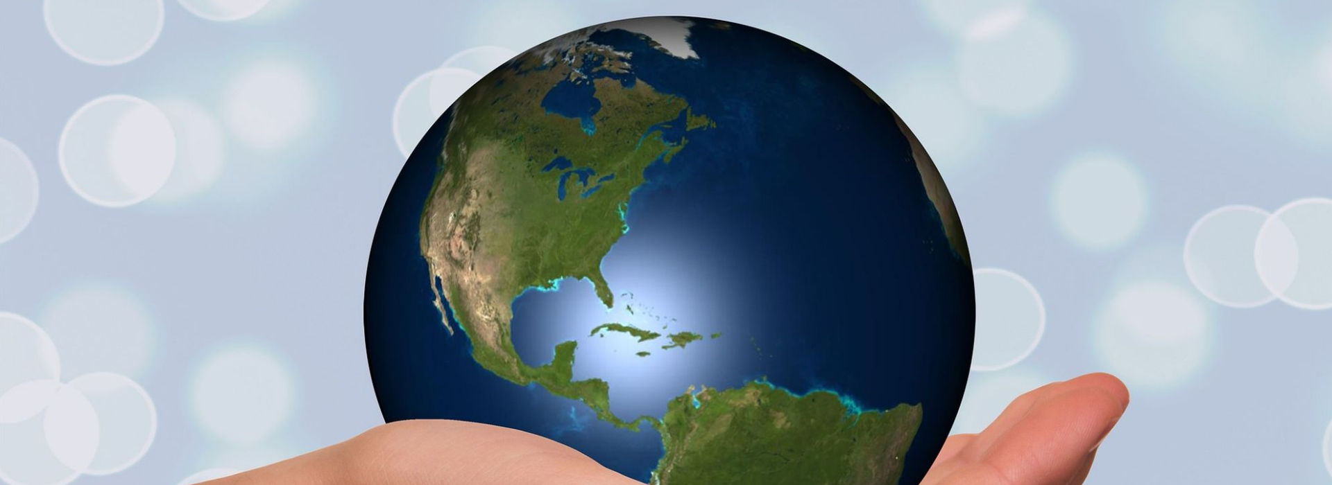 Planète terre déposée dans la paume d'une main avec arrière plan floue bleu pâle avec des bulles blanches.